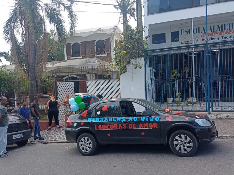 Carro de som decorado com a faixa Mensagem ao Vivo Loucuras de Amor estacionado na rua