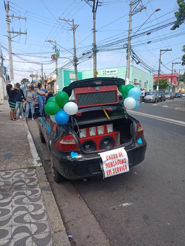 Carro com o porta-malas aberto, decorado com balões e placa de mensagem