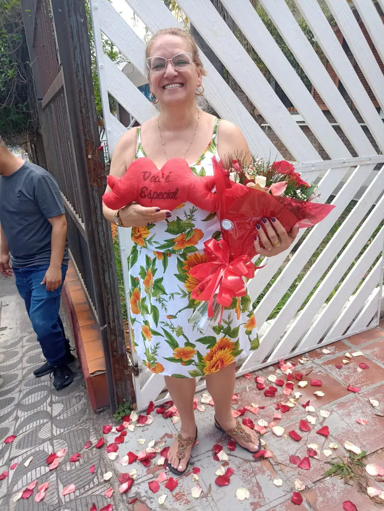 Homenageada segurando o coração de pelúcia vermelho no portão de casa