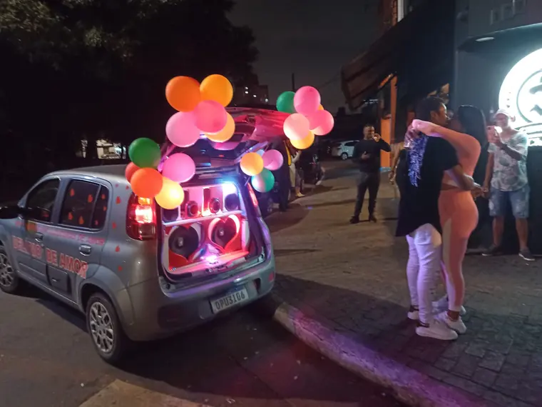 Casal se abraçando na calçada à noite com o carro de som decorado ao lado