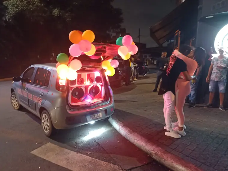 Mulher comemorando de braços abertos na rua ao lado do carro de som iluminado